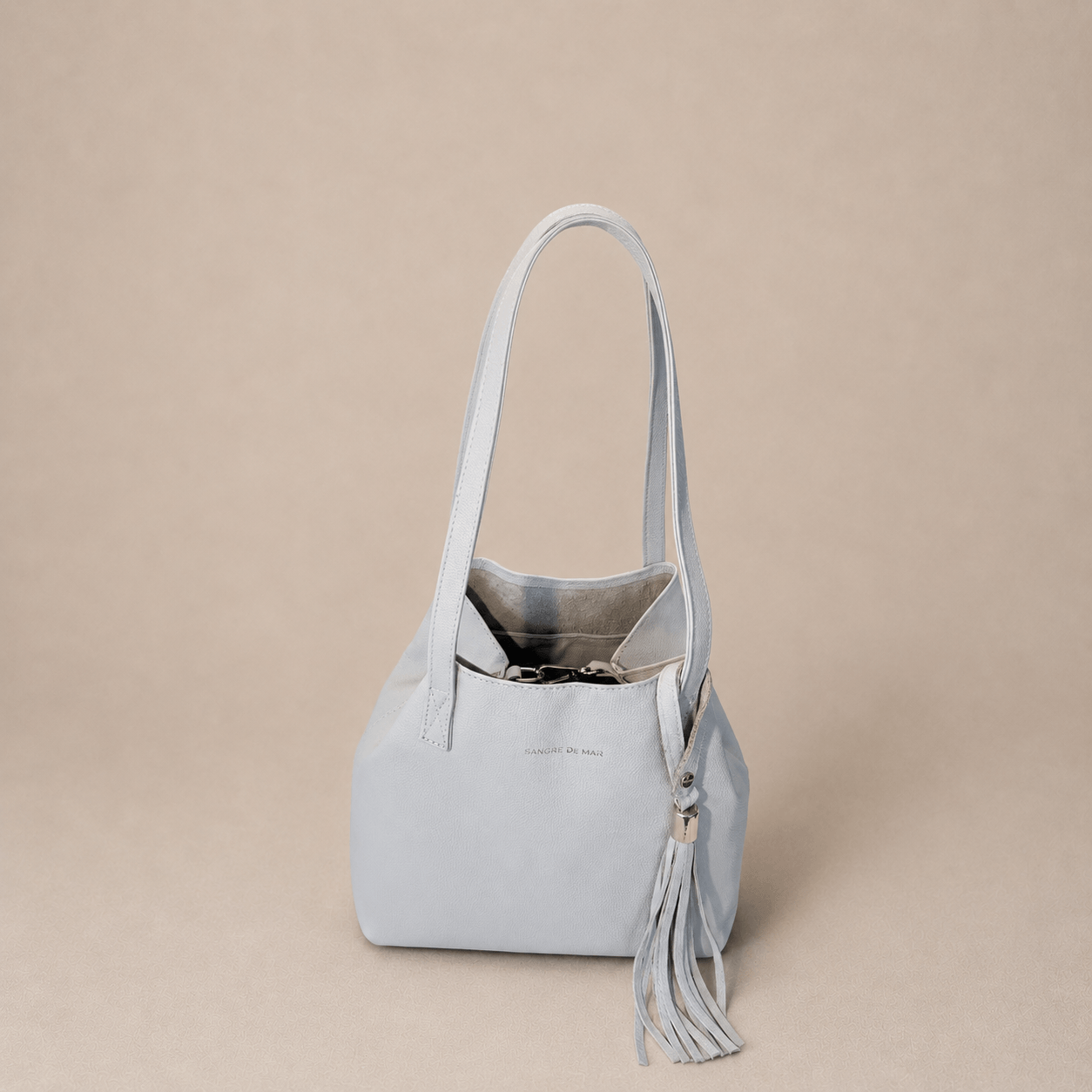 Off-white cold handbag with a tassel on a beige background