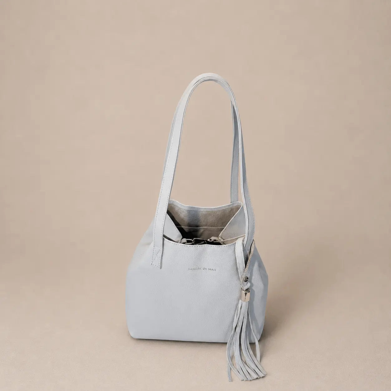 Off-white cold handbag with a tassel on a beige background