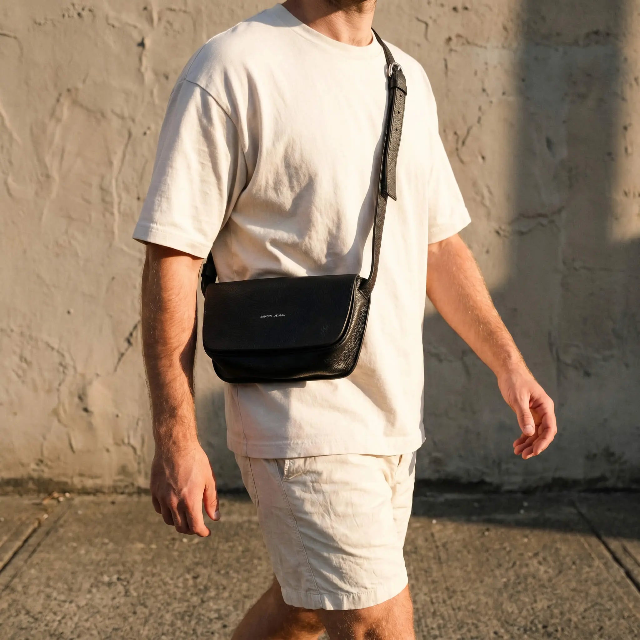 Person wearing a black crossbody bag against a textured wall.