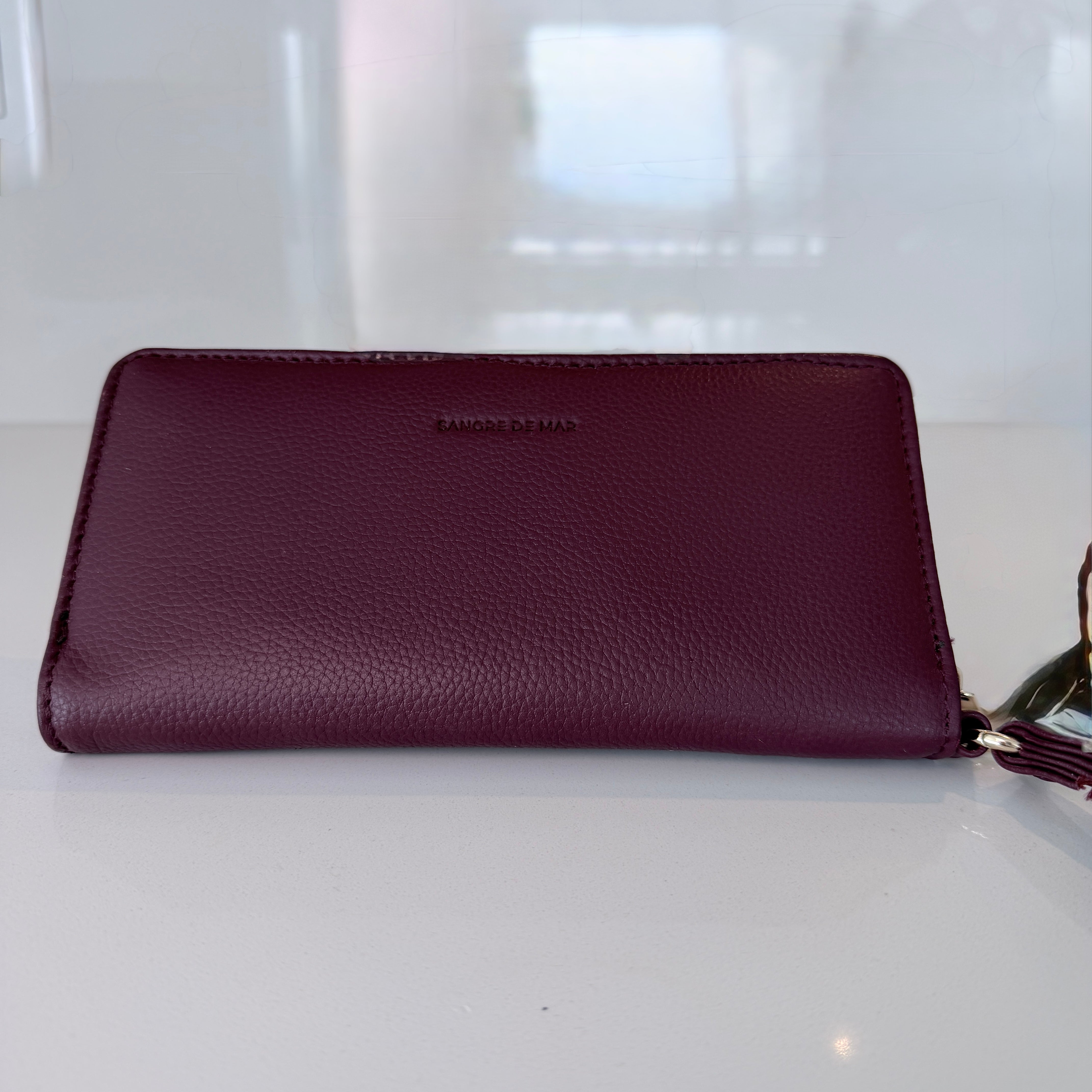 Merlot leather wallet with a Sangre de Mar logo on a white surface