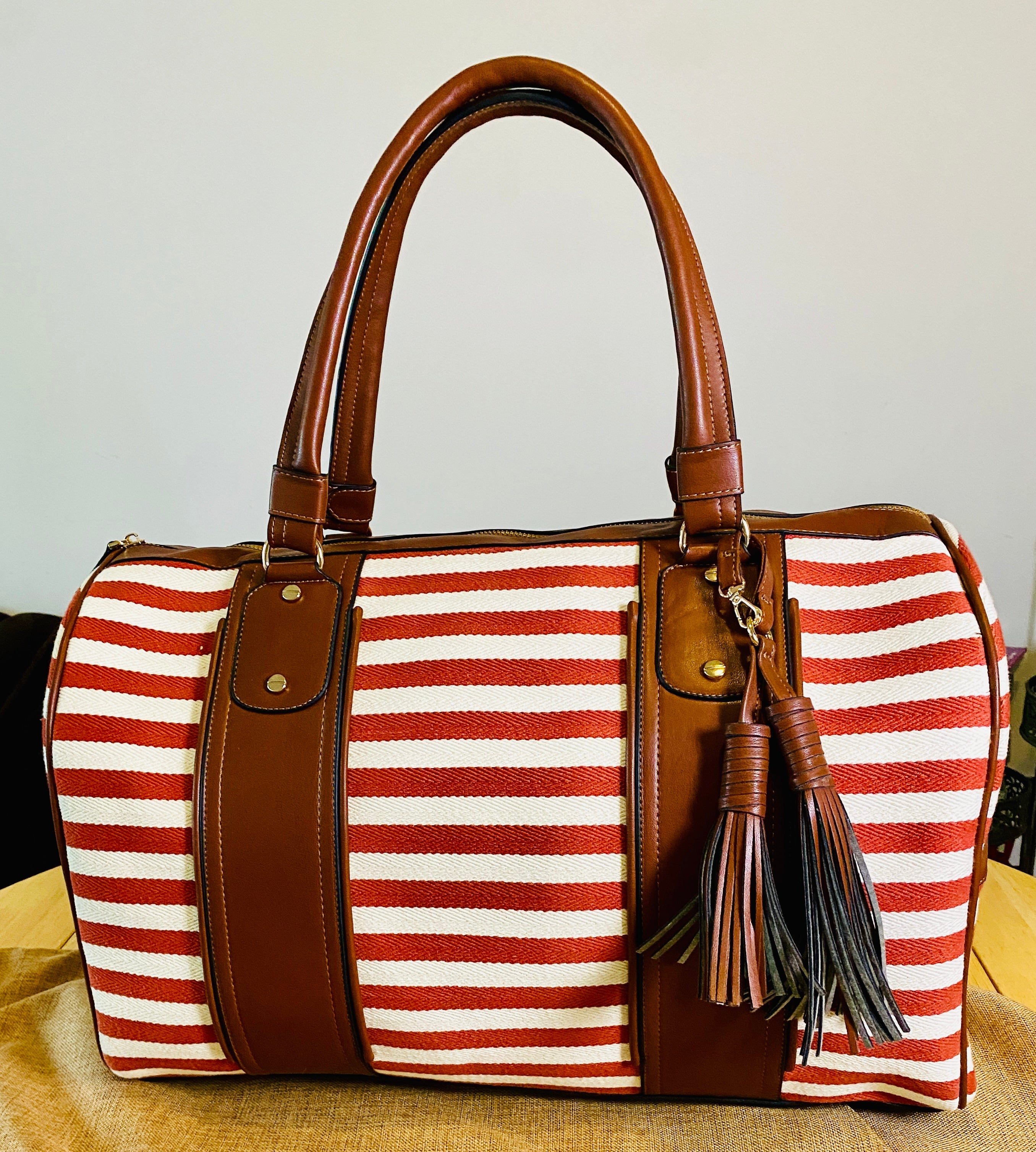 Striped handbag with brown handle and tassel on a beige surface, featuring 'Sangre de Mar' branding.
