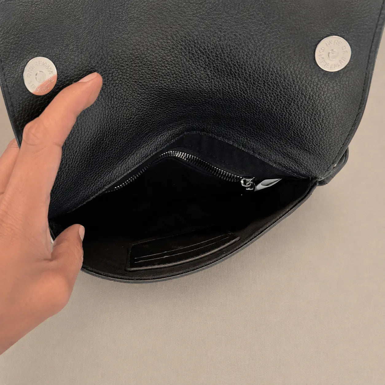 Black leather bag with a hand opening it on a beige background