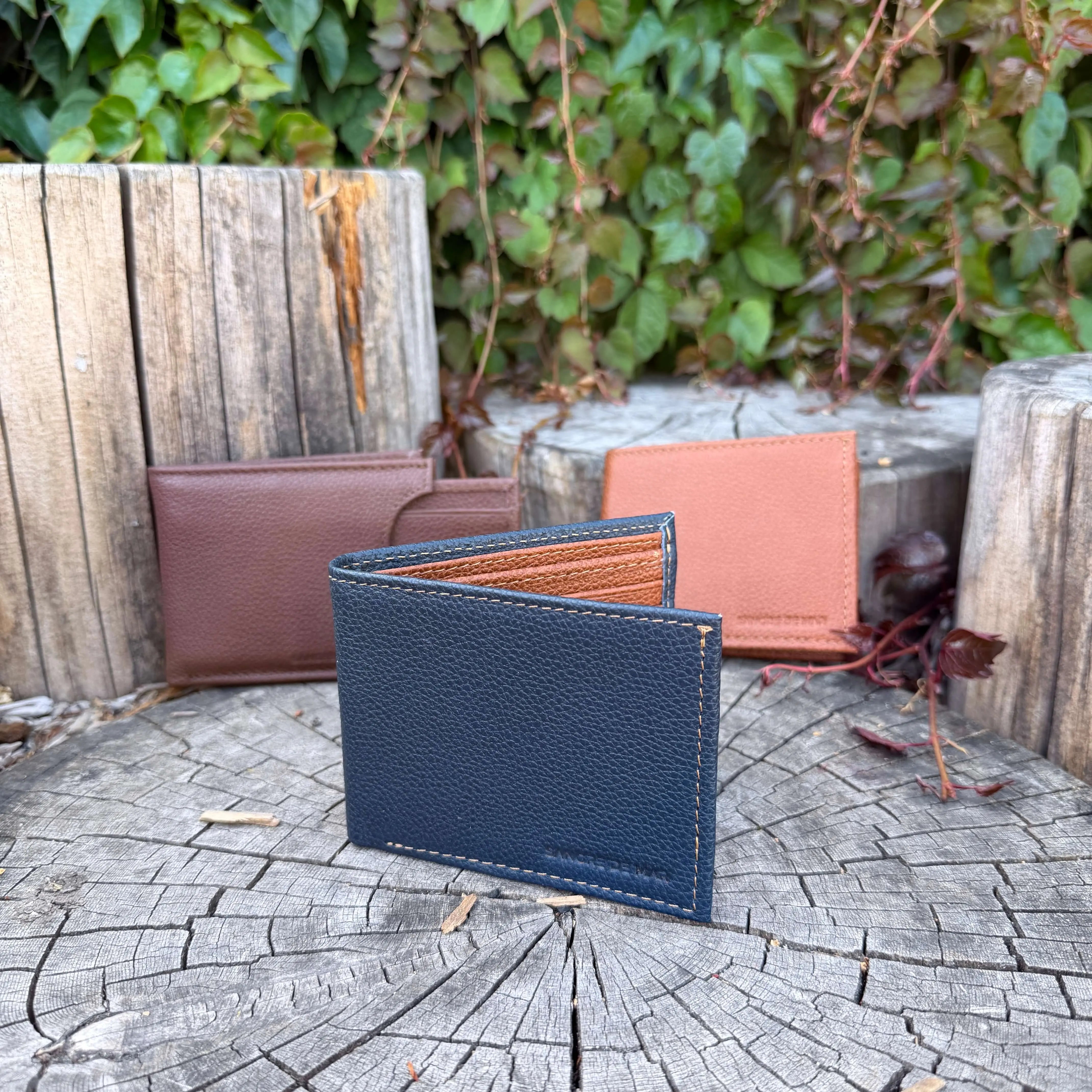 Three leather wallets in different colors on a wooden surface with a natural background