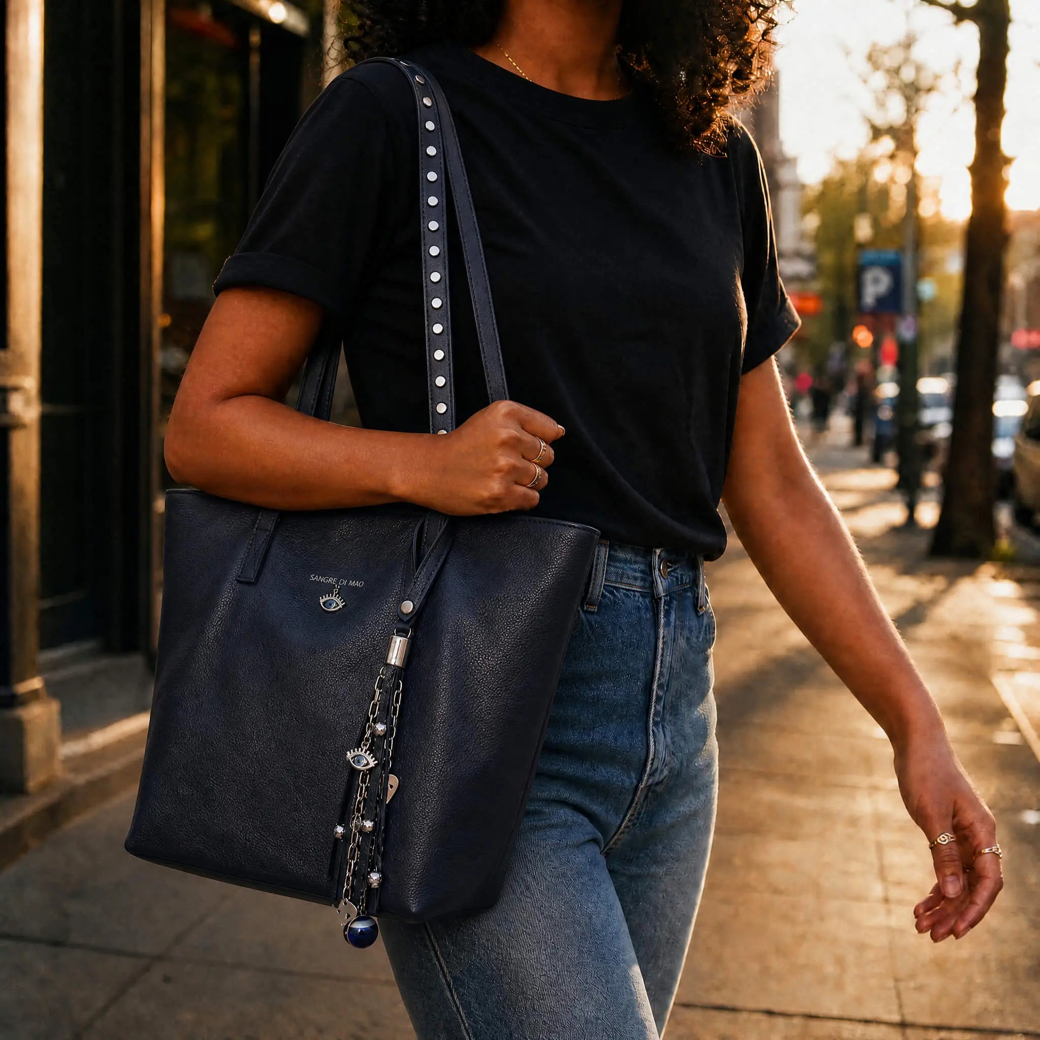 Woman wearing a tote bag in navy blue full grain leather with studs and blue amulets as charms